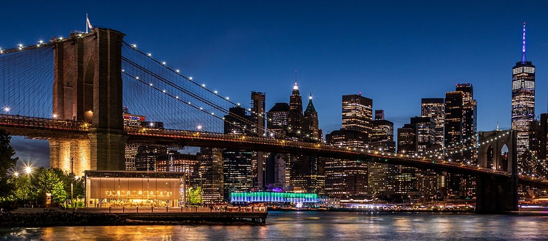 Night view of the Brooklyn Bridge and New York City skyline with illuminated skyscrapers and a vibrant waterfront, among the top things to do in the city.