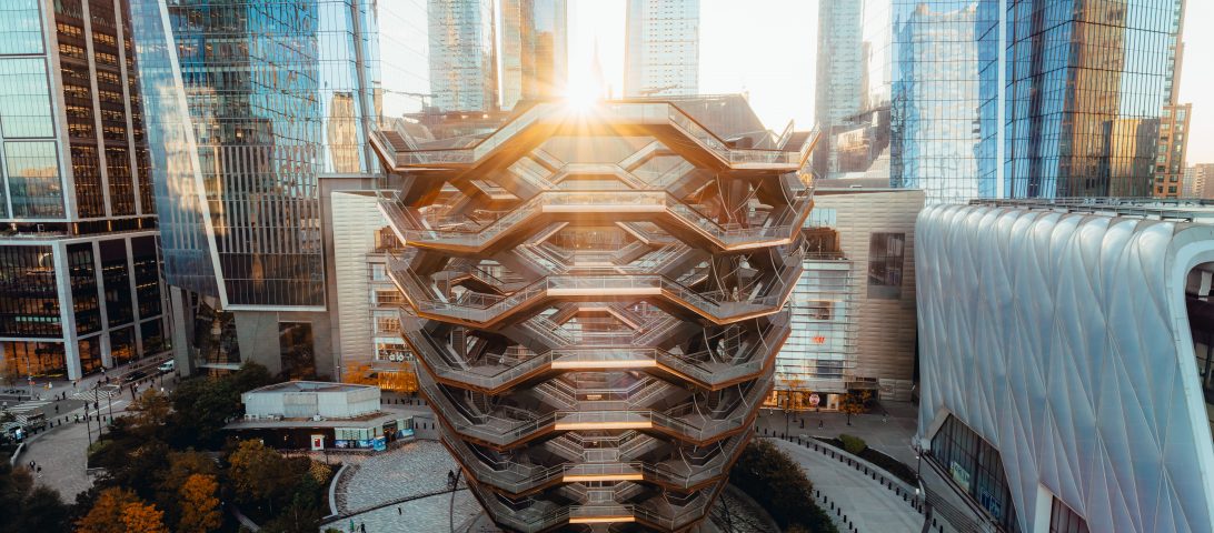 The Vessel, a honeycomb-like marvel and one of the intriguing things to do at Hudson Yards, is surrounded by towering skyscrapers. Sunlight gracefully peeks through its top.